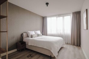Un dormitori amb un llit, una tauleta de nit i una finestra amb cortines.