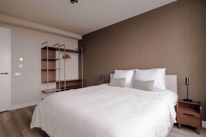 Ein modernes Schlafzimmer mit einem großen Bett, einem Nachttisch aus Holz, einer Nachttischlampe, einem Kleiderschrank mit offenen Regalen und einer Wandleuchte.