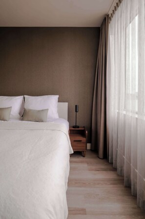 Ein Schlafzimmer mit einem großen Bett, einem Nachttisch, einer Lampe und transparenten Vorhängen.