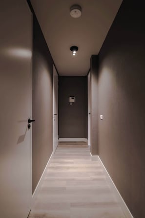 A hallway with a light fixture on the ceiling, a door on the left, and a wall-mounted intercom on the right. - City Center Penthouse w/ Free Parking & City Views (Rotterdam)