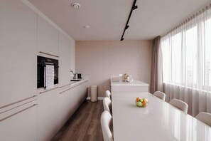 Una cocina moderna con horno integrado, una mesa de comedor con sillas y un amplio ventanal con cortinas.