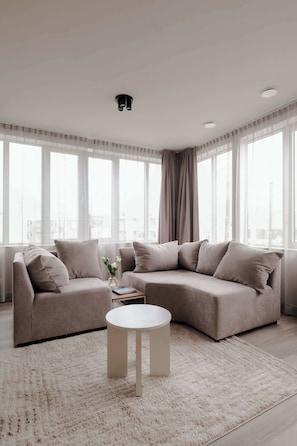 A modern living room with a sectional sofa, a round coffee table, and large windows with sheer curtains. - 2BR Penthouse Rotterdam City Centre (Rotterdam)