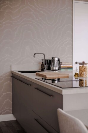 A kitchen with a modern design, featuring a stainless steel sink, a coffee maker, and a wooden cutting board. - 2BR Penthouse Rotterdam City Centre (Rotterdam)