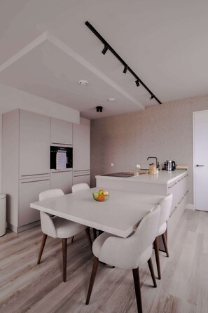 A modern kitchen with a white countertop, a dining table with chairs, and a kitchen island with a sink and stove. - 2BR Penthouse Rotterdam City Centre (Rotterdam)