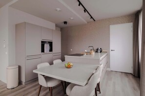 A modern kitchen with a dining area, white cabinetry, and a small island with a coffee maker. - 2BR Penthouse Rotterdam City Centre (Rotterdam)