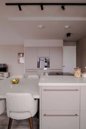 A modern kitchen with a central island, white cabinetry, and a dining area with a white chair and table. - 2BR Penthouse Rotterdam City Centre (Rotterdam)