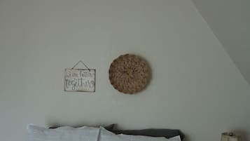 A bedroom with a bed, pillows, a wall-mounted basket, a sign, and a lamp.
