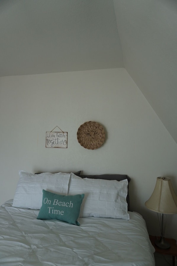 A bedroom with a bed, pillows, a wall-mounted basket, a sign, and a lamp.