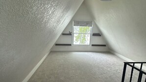 An attic room with a sloped ceiling, a window with a view of greenery, and a black metal railing. - Lakefront Retreat w/Dock +Walk to Surf District (Clear Lake)