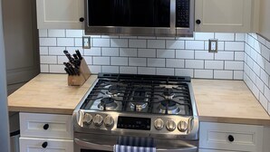 A kitchen with white cabinets, a stainless steel microwave, a gas stove, and a tiled backsplash. - Lakefront Retreat w/Dock +Walk to Surf District (Clear Lake)
