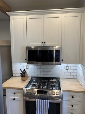 A kitchen with white cabinets, a stainless steel microwave, a gas stove, and a tiled backsplash.