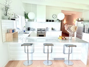 A modern kitchen with white cabinetry, a central island with bar stools, a gas stove, and a refrigerator.