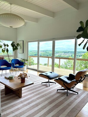 A modern living room with a large window, a blue chair, a black lounge chair, and a wooden coffee table. - Luxury Mid Century Home on Hudson Waterfront Bluff. 4 bed/3 bath (Highland)