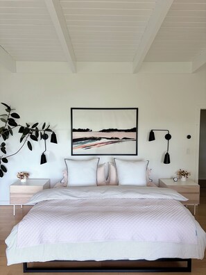 Une chambre à coucher comprenant un lit, deux tables de chevet, une lampe fixée au mur, un tableau encadré et une plante.