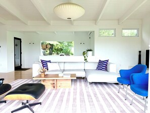 Ein modernes Wohnzimmer mit einem weißen Sofa, blauen Sesseln, einem Couchtisch und einem Streifenmuster-Teppich.
