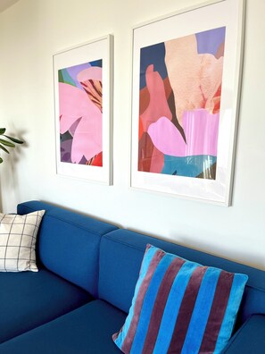 Un sofá azul con un cojín a rayas y dos cuadros abstractos en la pared.
