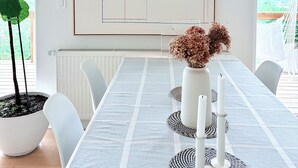 A dining area with a long table, white chairs, a large abstract painting, a potted plant, and a vase with dried flowers. - Luxury Mid Century Home on Hudson Waterfront Bluff. 4 bed/3 bath (Highland)