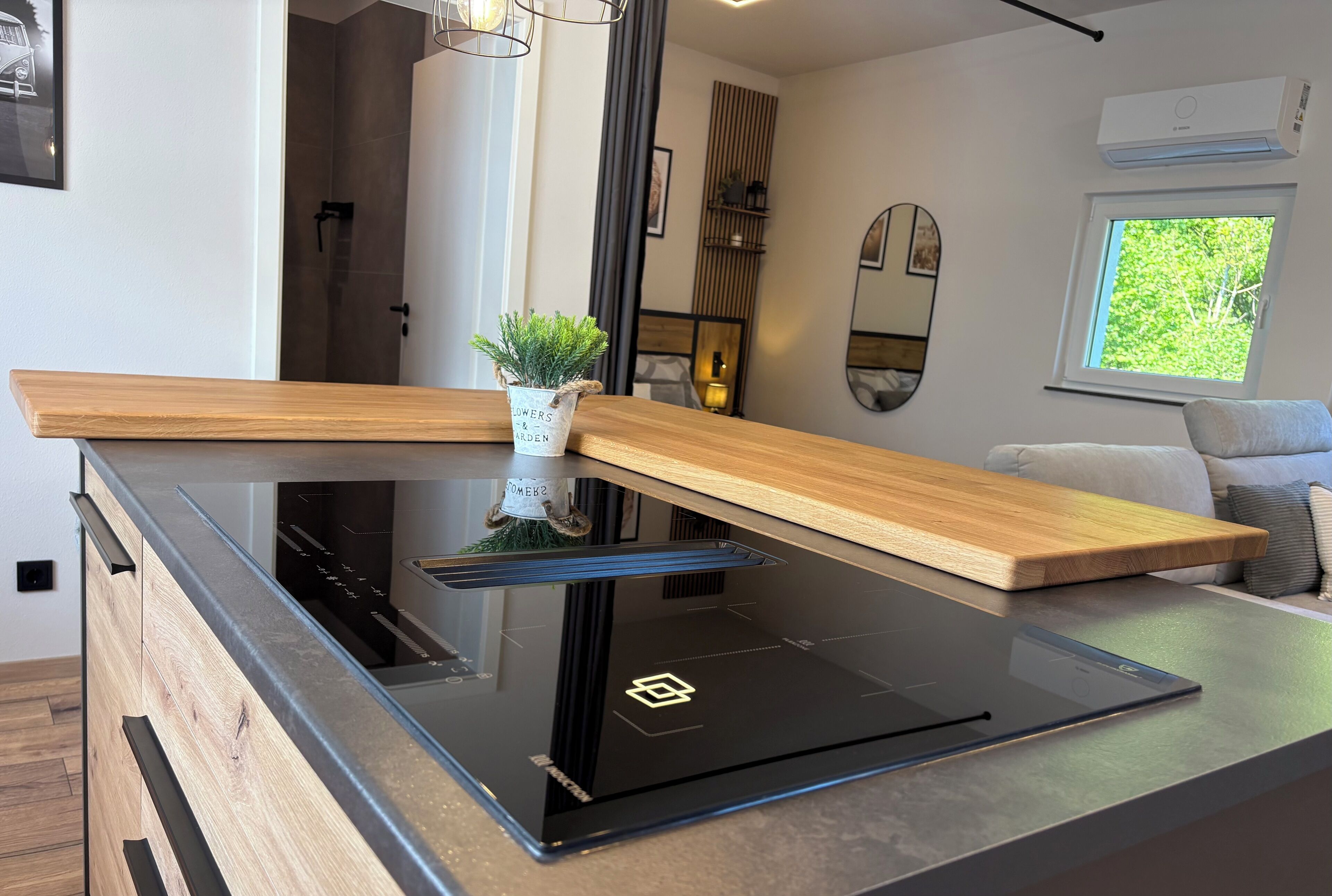 A modern kitchen with a glass cooktop, wooden countertop, and a small potted plant.