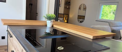A modern kitchen with a glass cooktop, wooden countertop, and a small potted plant.