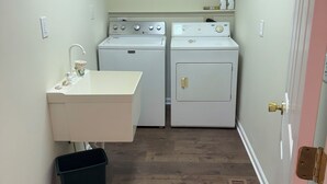 A laundry room with two washing machines, a sink, and a trash bin. - Quiet, serene 3-bedroom house with in charming Owingsville, Kentucky. (Owingsville)