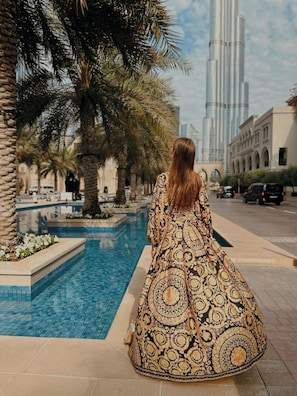 A woman standing by a pool with palm trees and a tall building in the background.