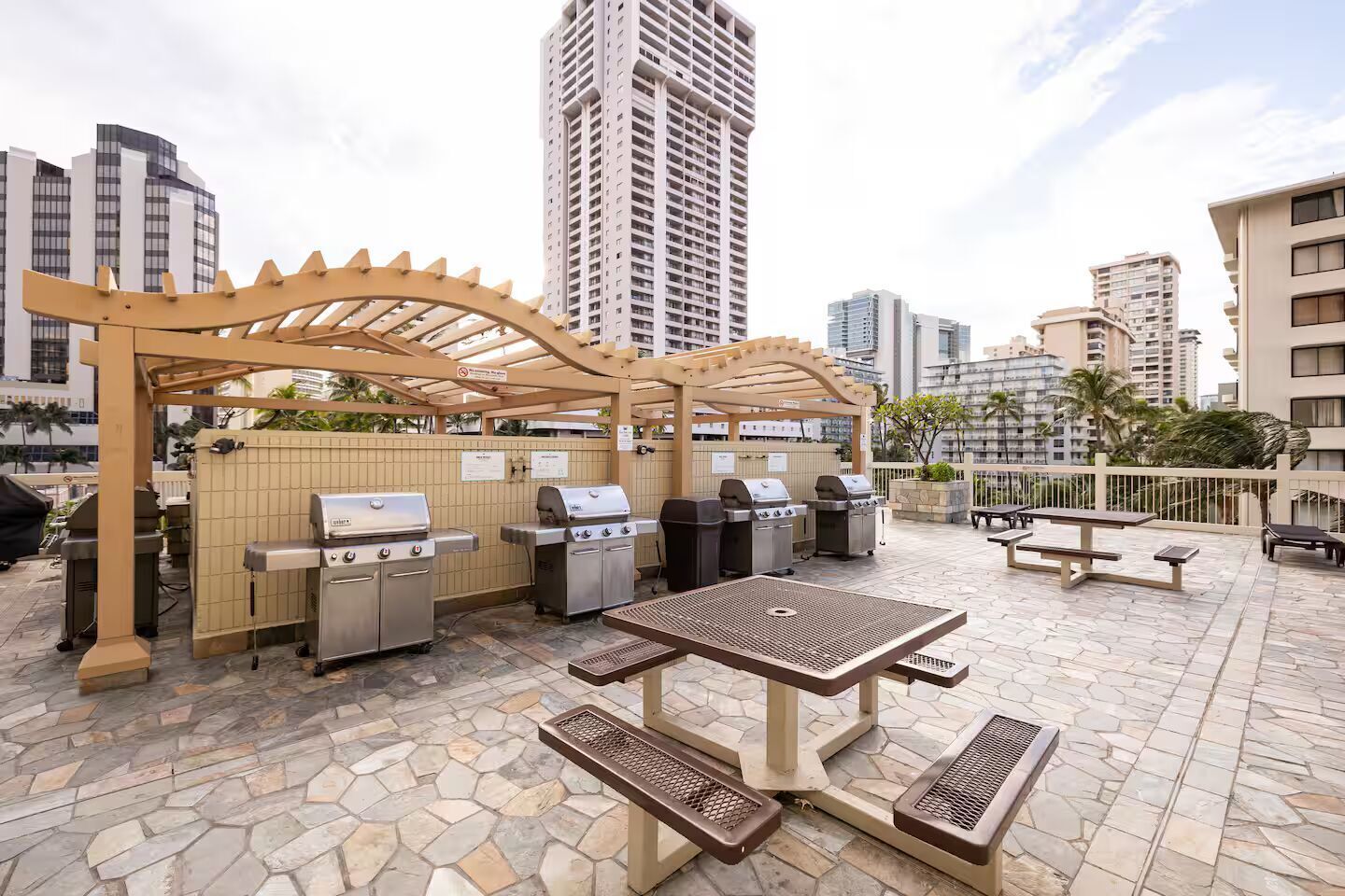 Un patio al aire libre con estaciones de parrillada, una mesa y bancos.