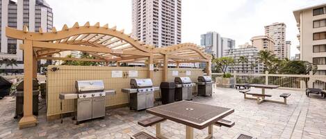 Un patio al aire libre con estaciones de parrillada, una mesa y bancos.