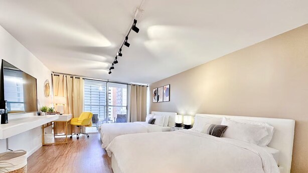Habitación de hotel con una cama grande, un escritorio con silla, televisor y ventana con cortinas.