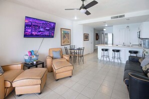 A modern living room with a flat-screen TV, a dining area with a table and chairs, a kitchen with a bar and stools, and a ceiling fan. - Beachfront 1BR Penthouse Sonoran Spa N805 (Puerto Peñasco)