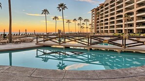 A hotel with a pool, palm trees, and a view of the ocean at sunset. - Beachfront 1BR Penthouse Sonoran Spa N805 (Puerto Peñasco)