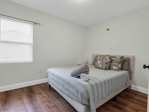 A bedroom with a bed, a window with blinds, a nightstand, and a door. - Beautiful 3-bedroom home with pool near beaches and attractions (Palmetto)