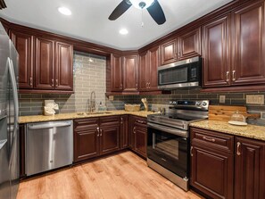 A kitchen with dark wooden cabinets, stainless steel appliances, and a tiled backsplash. - Beautiful 3-bedroom home with pool near beaches and attractions (Palmetto)