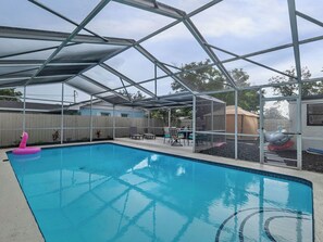 A covered outdoor swimming pool with a glass enclosure, a lounge area with chairs, and a flamingo float. - Beautiful 3-bedroom home with pool near beaches and attractions (Palmetto)