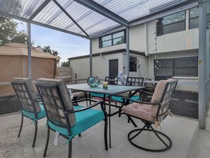 Eine überdachte Terrasse mit Tisch und Stühlen, im Hintergrund ein Haus und ein klarer Himmel.