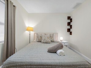 A bedroom with a bed, a bedside lamp, a nightstand, and a wall-mounted shelf. - Beautiful 3-bedroom home with pool near beaches and attractions (Palmetto)