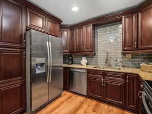 A kitchen with dark wood cabinets, stainless steel appliances, and a tiled backsplash. - Beautiful 3-bedroom home with pool near beaches and attractions (Palmetto)