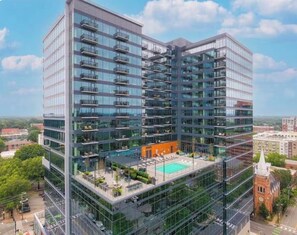 A high-rise building with multiple balconies, a rooftop pool, and a mix of glass and brick facade. - Cozy 1-bedroom apartment in fantastic Raleigh with AC and gym access (Raleigh)
