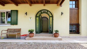 A building with a green door, a bench, and two potted plants on the steps. - Papavero Room with Mountain View, Shared Garden and Wi-Fi (Bivedo-Larido-Marazzone)