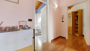 A hallway with a wooden floor, a white door, and a wooden shelf unit with books. - Papavero Room with Mountain View, Shared Garden and Wi-Fi (Bivedo-Larido-Marazzone)
