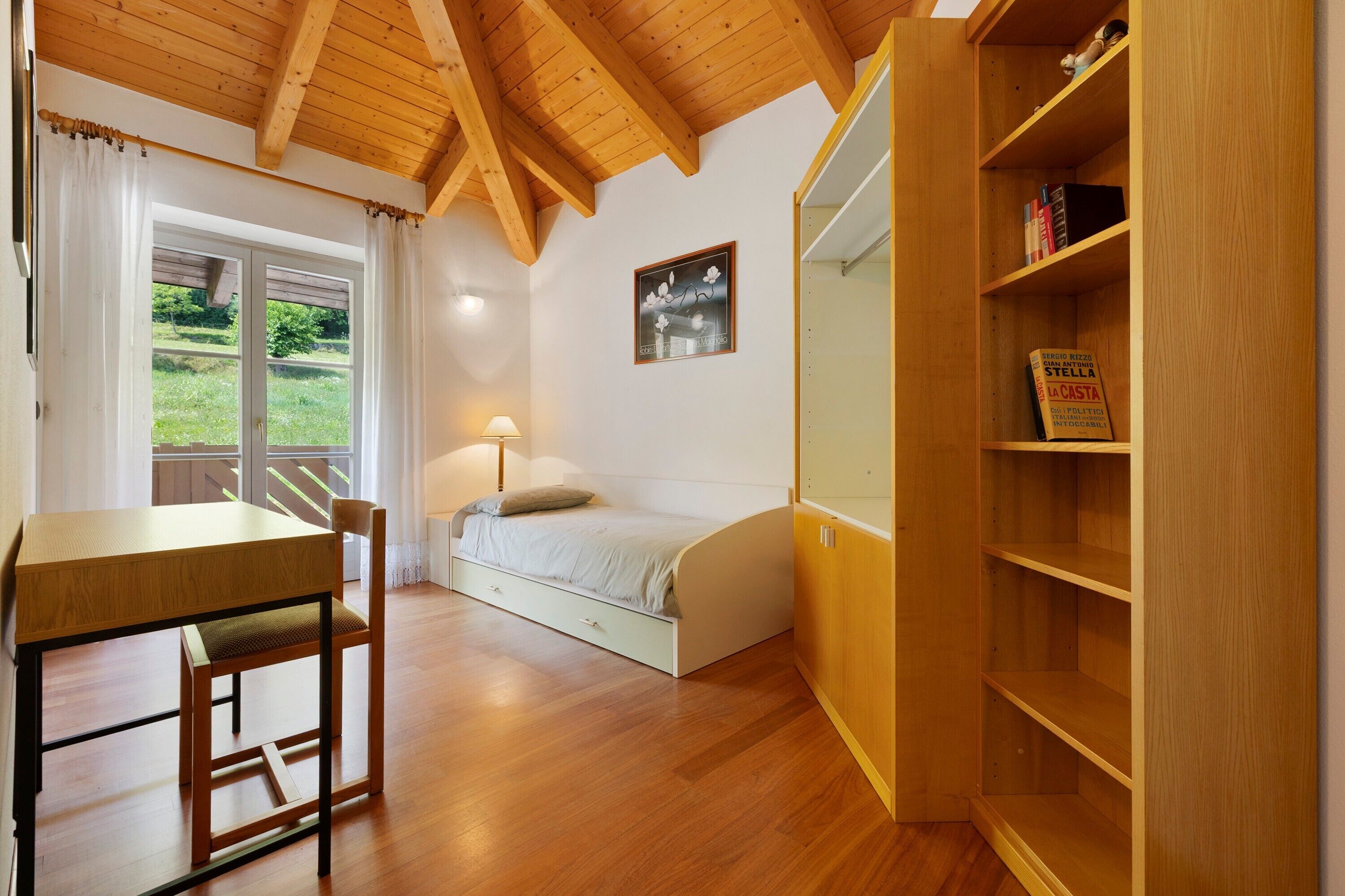 A bedroom with a wooden desk, a bed, a nightstand, and a bookshelf.