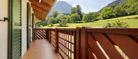 A wooden balcony with a view of a green landscape and mountains.