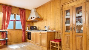 Eine Holzküche mit Einbauofen, Mikrowelle und Spüle. Ein Stuhl mit roter Sitzkissen sowie eine Schrank mit Glastüren.