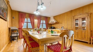 Ein Esszimmer mit Holztisch, gedeckt für vier Personen, Stühle mit roten Kissen, einer Küchenzeile mit Schränken und einer Hängeleuchte.