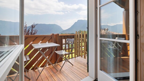 Eine Holzterrasse mit Tisch und Stühlen, eine Glastür und Blick auf die Berge.