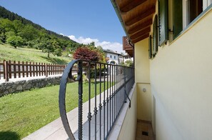 A balcony with a metal railing overlooking a grassy area with a stone wall and a wooden fence.