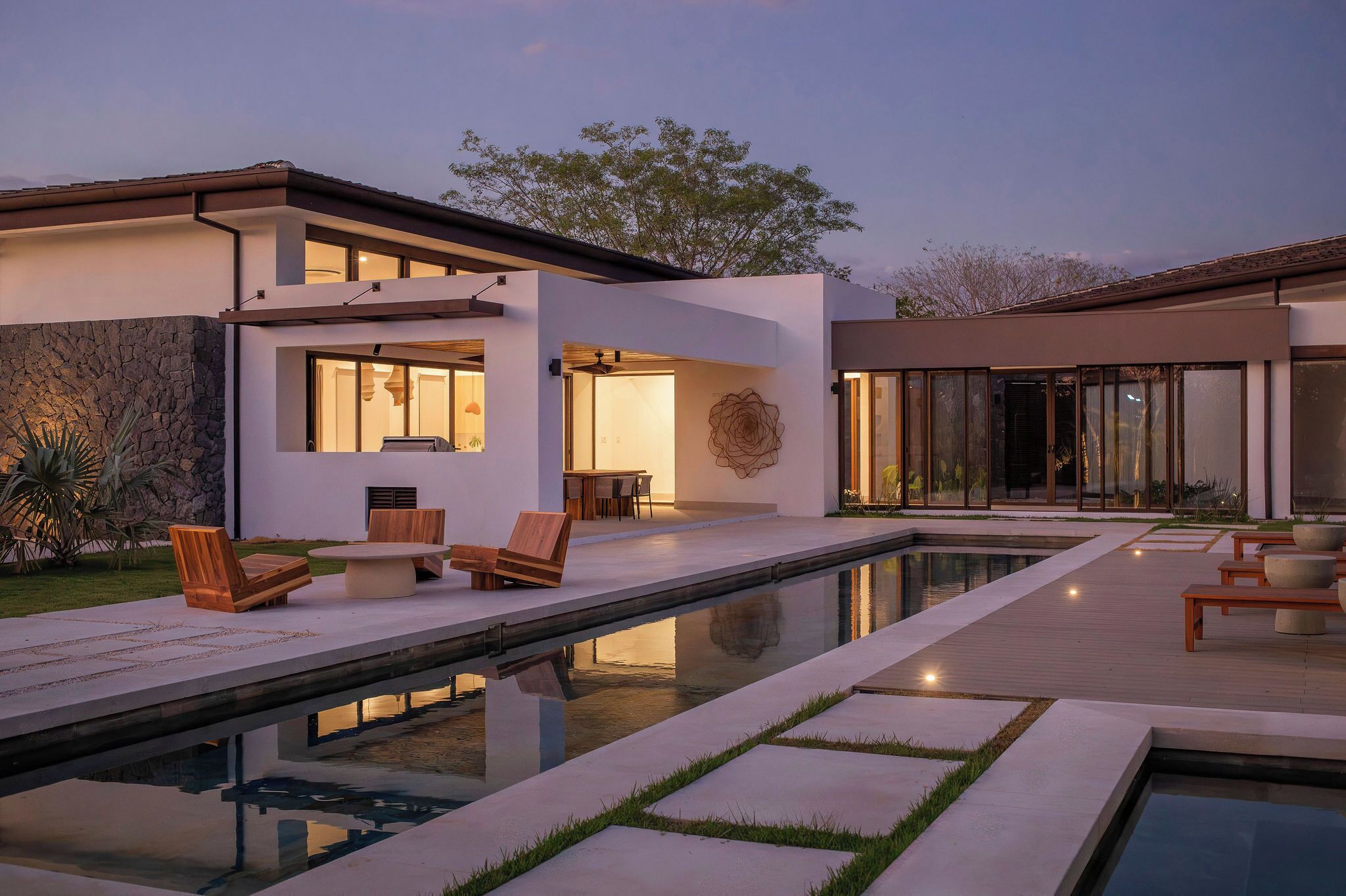 A modern house with a swimming pool, outdoor seating, and a stone wall.