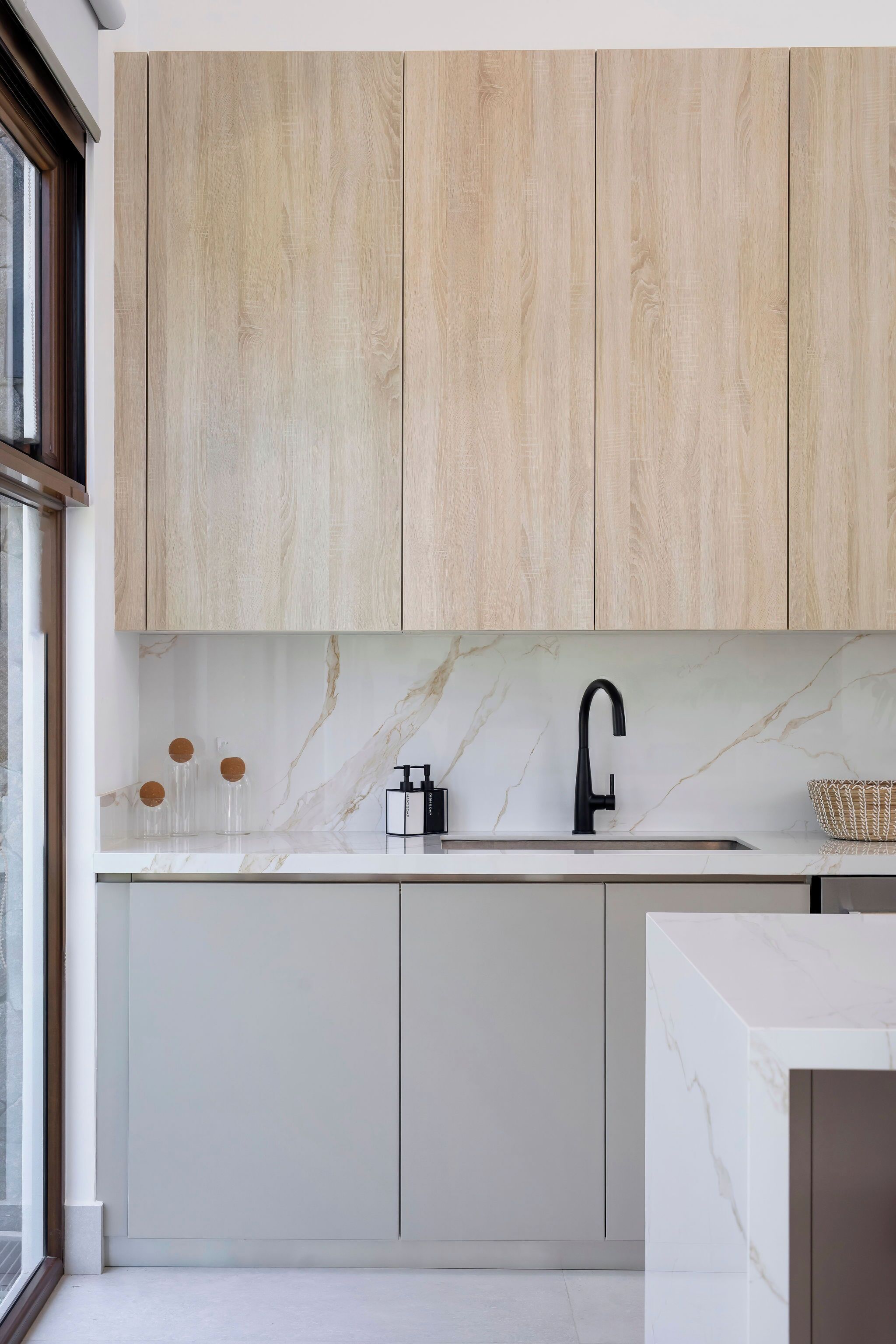A modern kitchen with light wood cabinets, a marble countertop, and a black faucet.