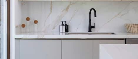 A modern kitchen with light wood cabinets, a marble countertop, and a black faucet.