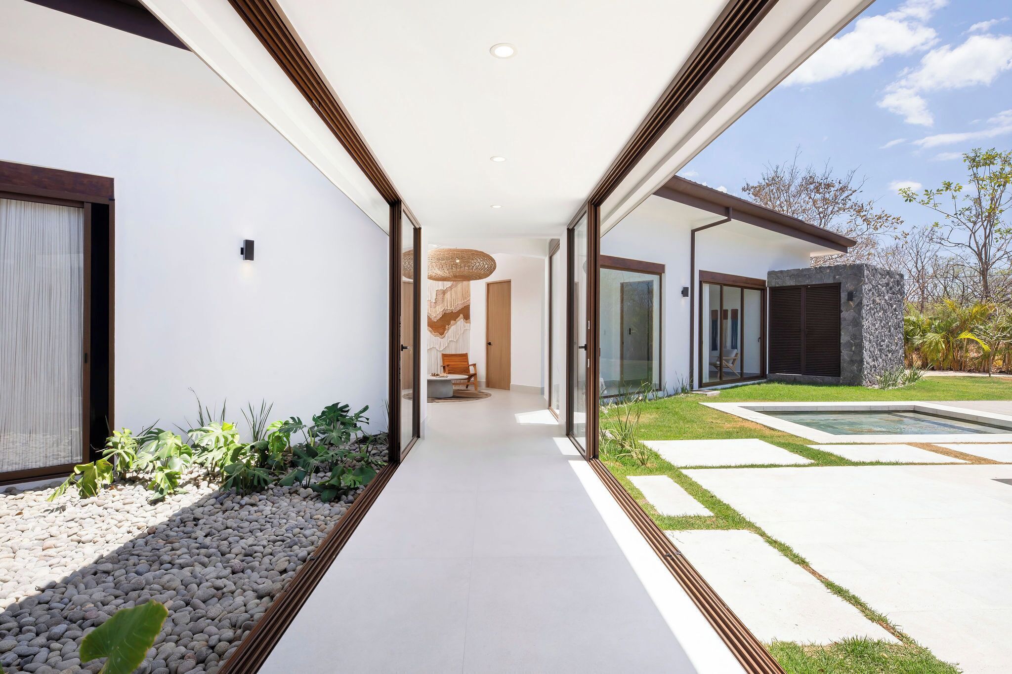 A modern house with a covered walkway, a stone wall, and a pool.