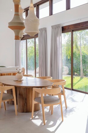 Ein moderner Essbereich mit einem großen Holztisch, mehreren Stühlen und hängenden Gewebeleuchten.